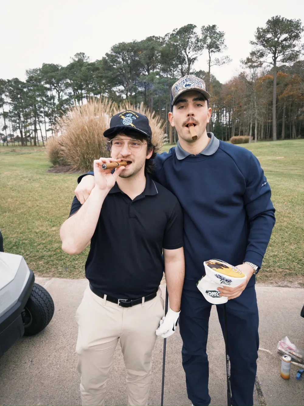 Two players, cigars lit, pampas grass behind