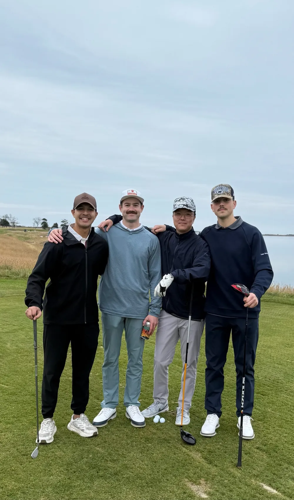 Four of the group arm in arm on the tee by the water