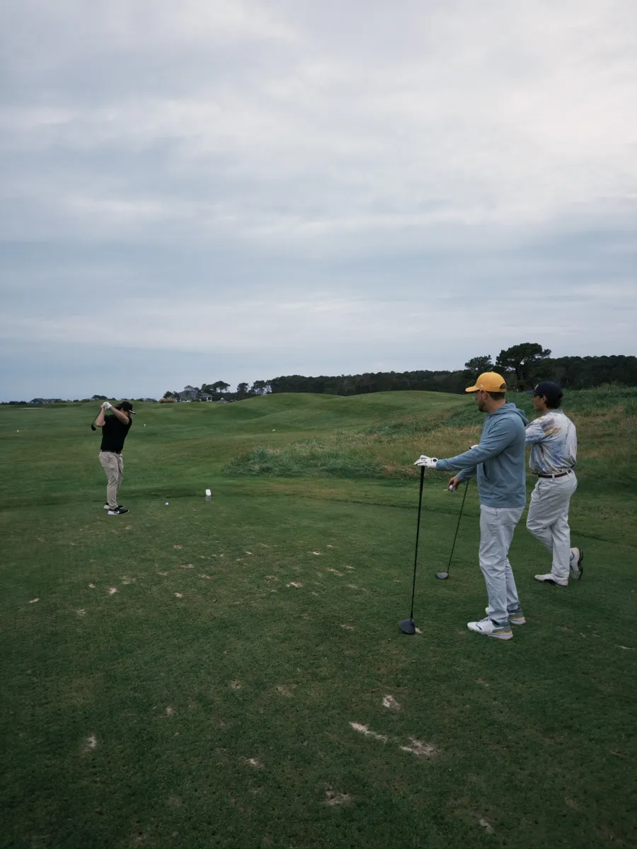 Three on the tee, one mid-swing, dunes rolling toward the clubhouse