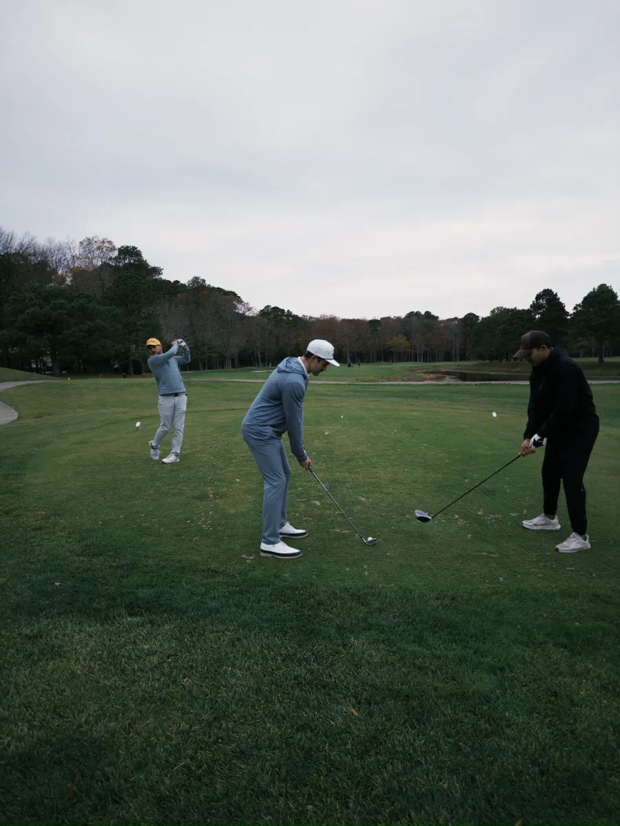 A fairway spread out, drivers out under a grey autumn sky
