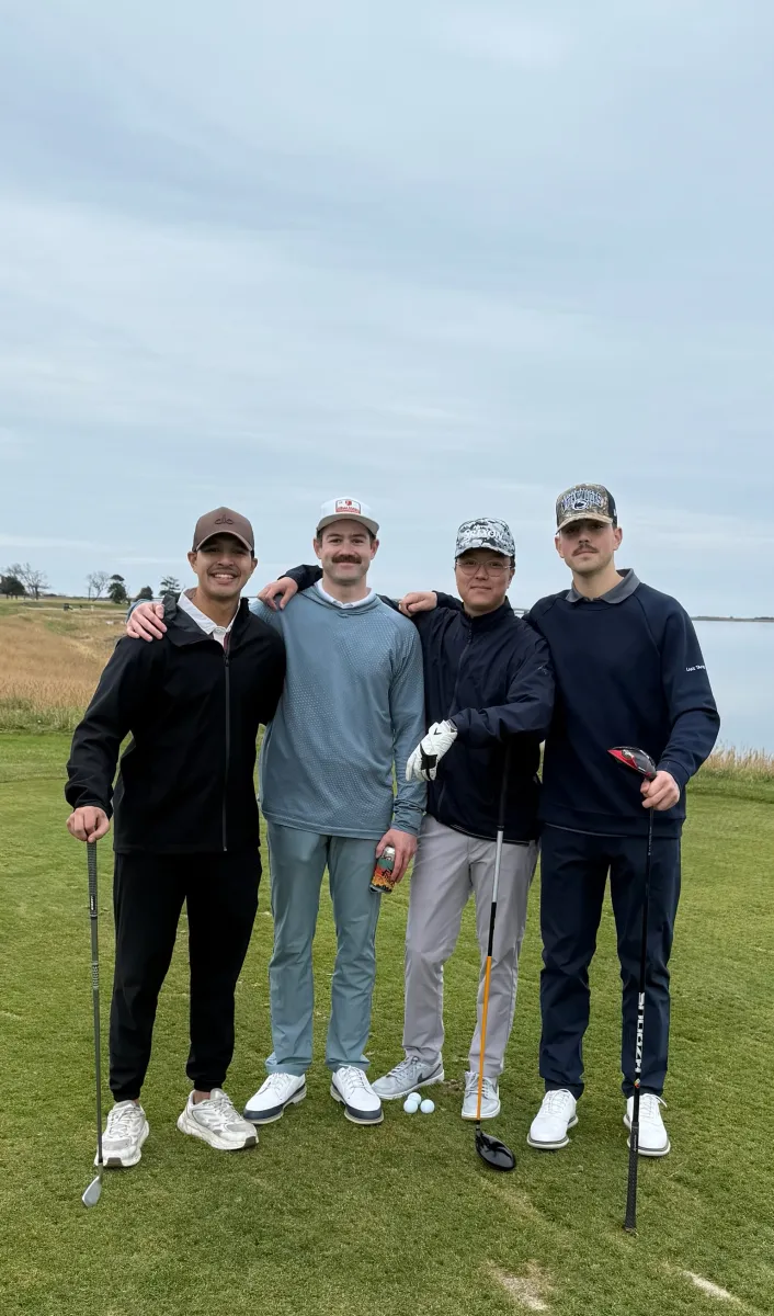 Four arm in arm on the tee box, the bay behind them